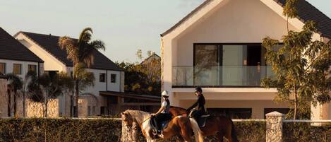 A modern house with a balcony, a horse, and riders.