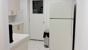 A compact kitchen with white cabinets, a refrigerator, a trash bin, and a door with a window. - Modern 1BR • Private Entry • Kitchen & W/D (Oshawa)