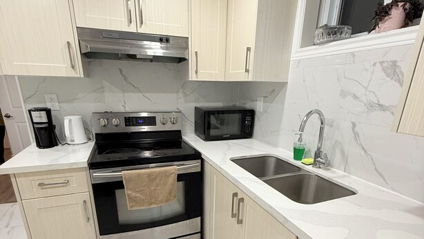 A modern kitchen with light-colored cabinets, a stainless steel range, a microwave, and a sink with a faucet. - Modern 1BR • Private Entry • Kitchen & W/D (Oshawa)