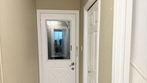 A narrow hallway with a white door at the end, beige walls, and a tiled floor. - Modern 1BR • Private Entry • Kitchen & W/D (Oshawa)