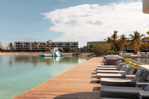 A poolside area with lounge chairs, a wooden deck, and a building in the background. - NOK Modern 1BR Apartment with Terrace in Vistacana (Punta Cana)