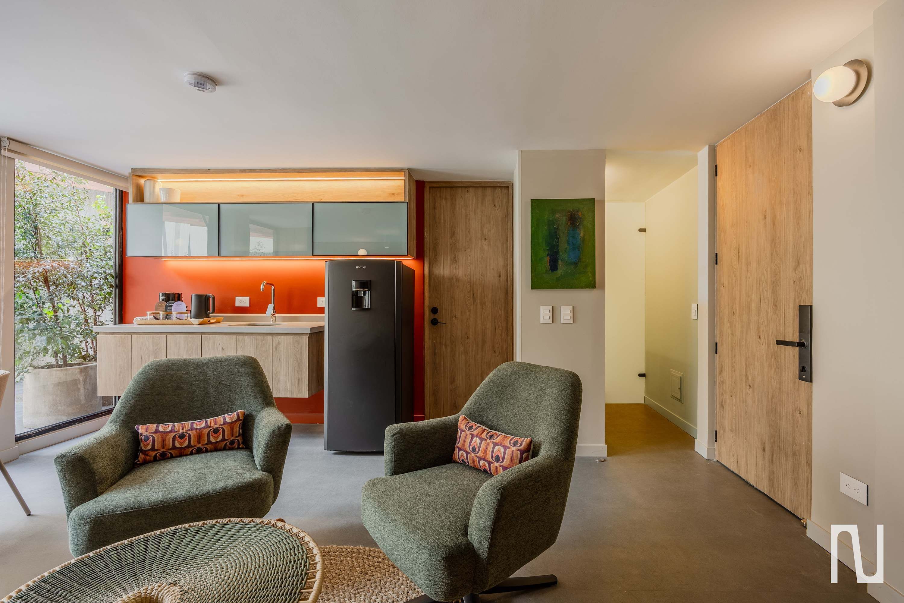 Een moderne woonkamer met twee fauteuils, een keuken met een koelkast, en een houten deur.