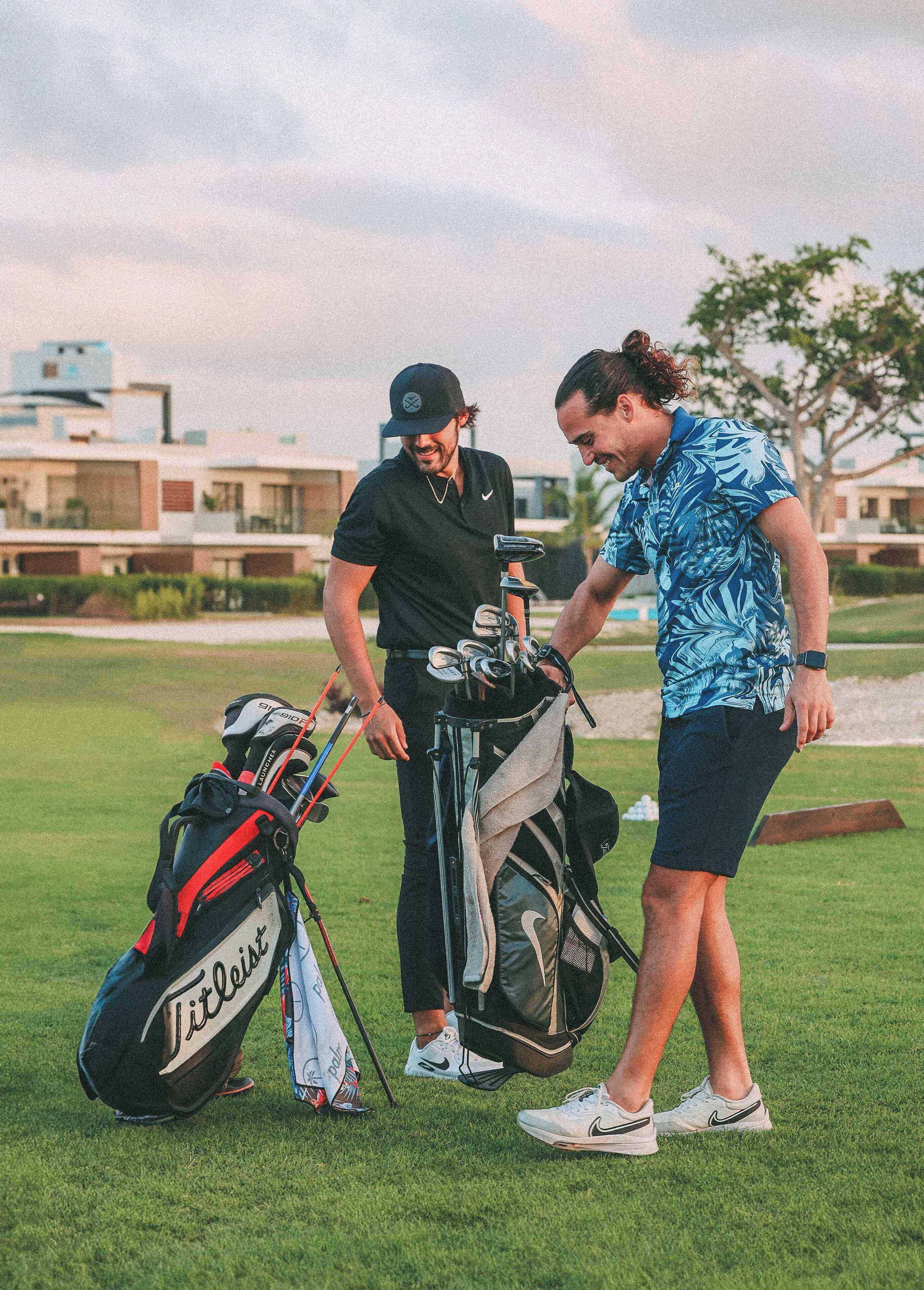Två personer står på en golfbana med golfbagar och golfklubbor.