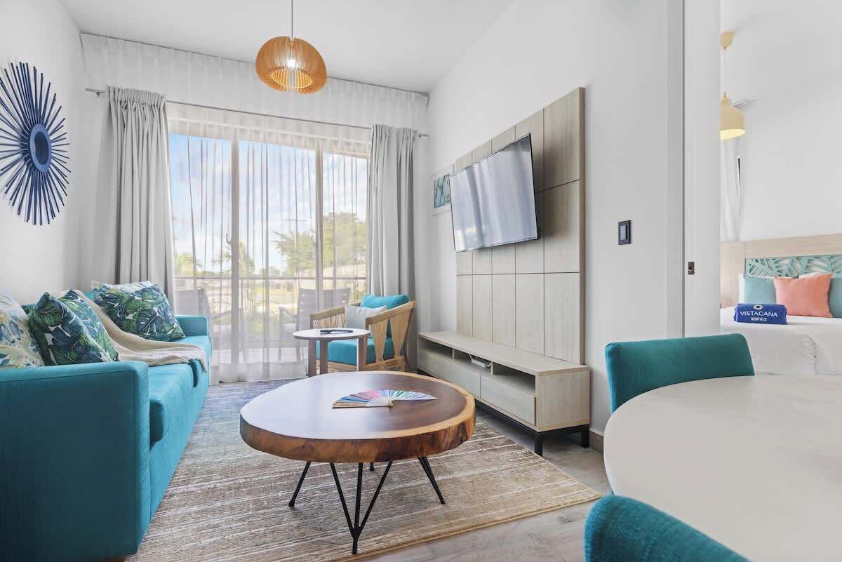 Ein modernes Hotelzimmer mit Sofa, rundem Couchtisch, Fernseher und Blick durch große Fenster.