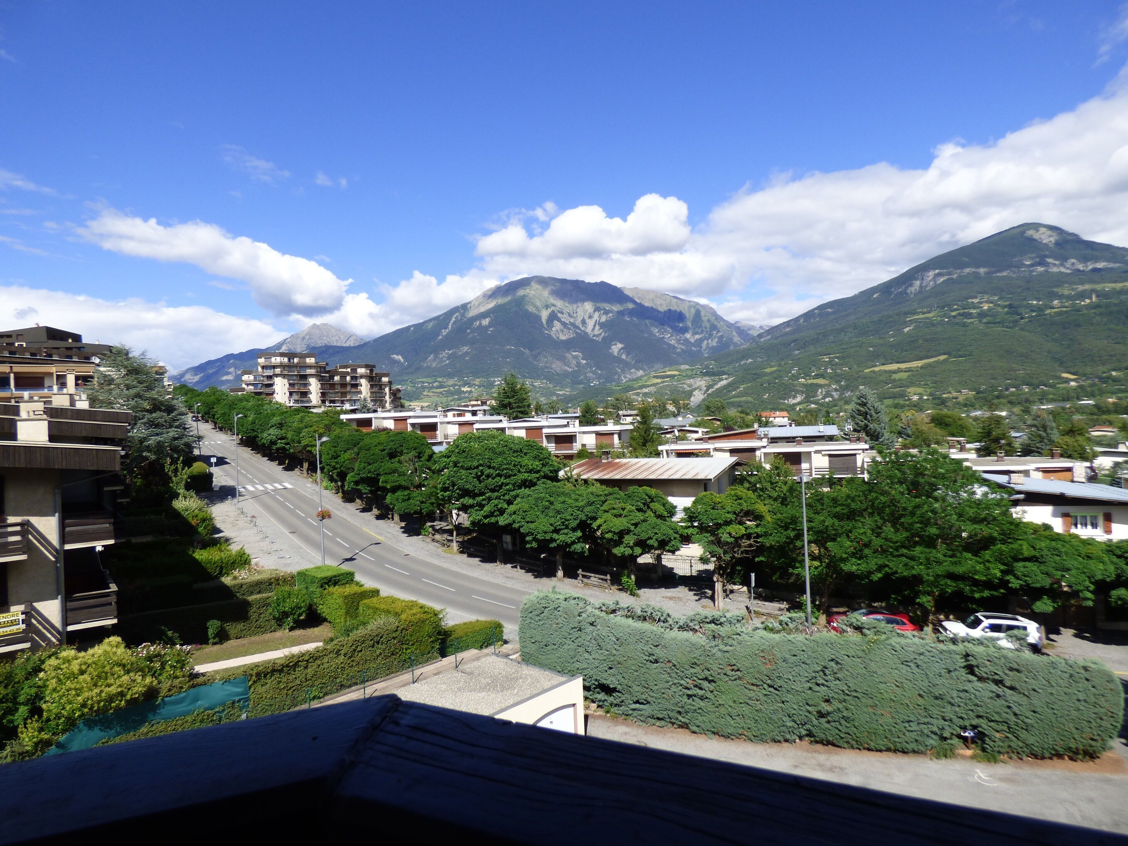 Un quartier résidentiel avec une route, des bâtiments et des montagnes en arrière-plan.