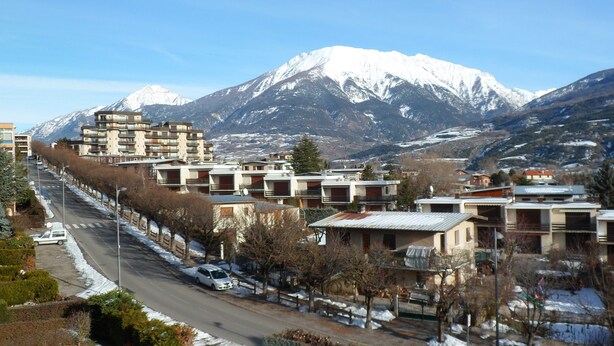 A residential area with modern buildings, a snow-covered mountain in the background, and a clear sky. - "Aux Aurores" – Charming Apartment with Mountain View and Balcony (Embrun)