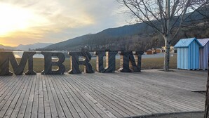 A wooden deck with large letters spelling 'EMBRUN' and a view of a lake and mountains in the background. - "Aux Aurores" – Charming Apartment with Mountain View and Balcony (Embrun)