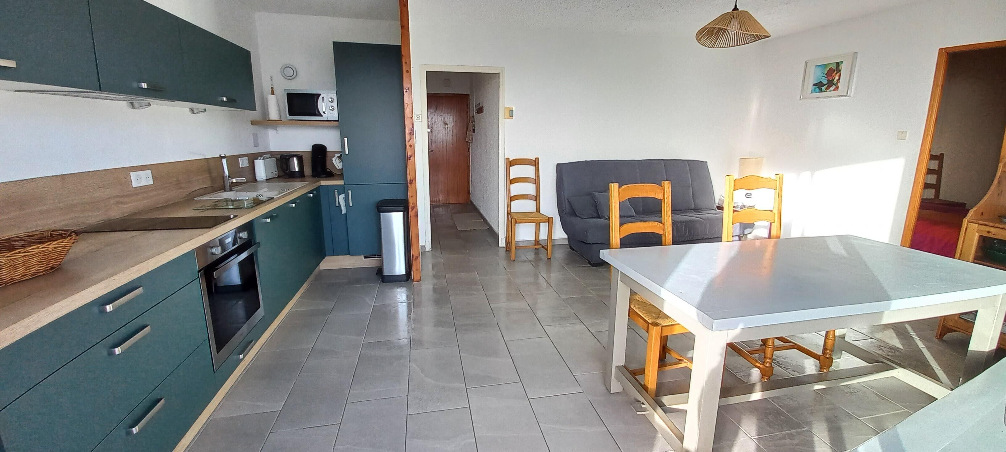 A compact kitchen with a microwave, toaster, and sink. There is a dining table with chairs and a sofa in the living area.