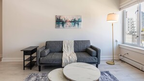Ein modernes Wohnzimmer mit einem grauen Sofa, einem runden Marmortisch, einem Bild an der Wand und einer Stehlampe.