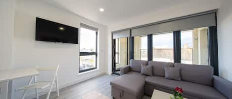 A modern living room with a sectional sofa, a flat-screen TV mounted on the wall, a small table, and a chair.