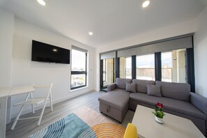 Ein modernes Wohnzimmer mit einer Eckcouch, einem Flachbildfernseher an der Wand, einem kleinen Tisch und einem Sessel.