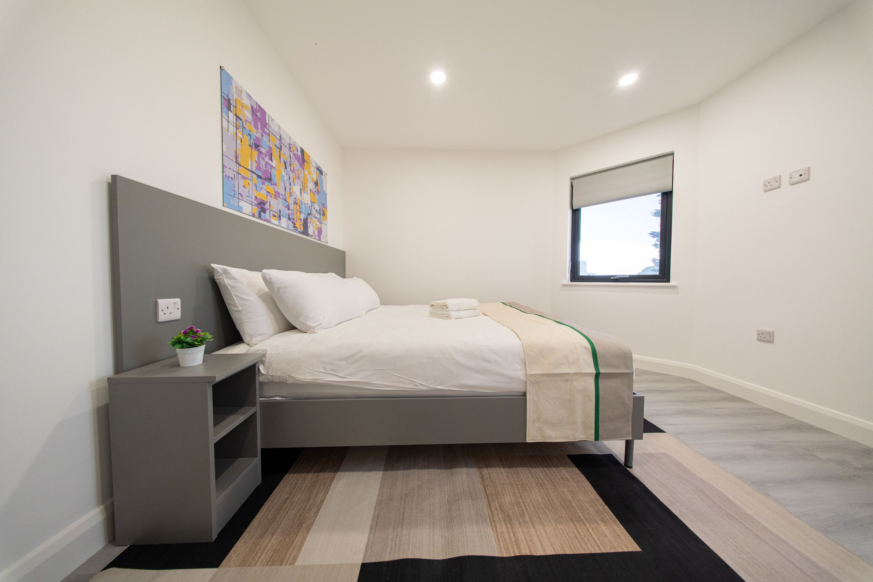 A modern bedroom with a bed, bedside table, and a window.