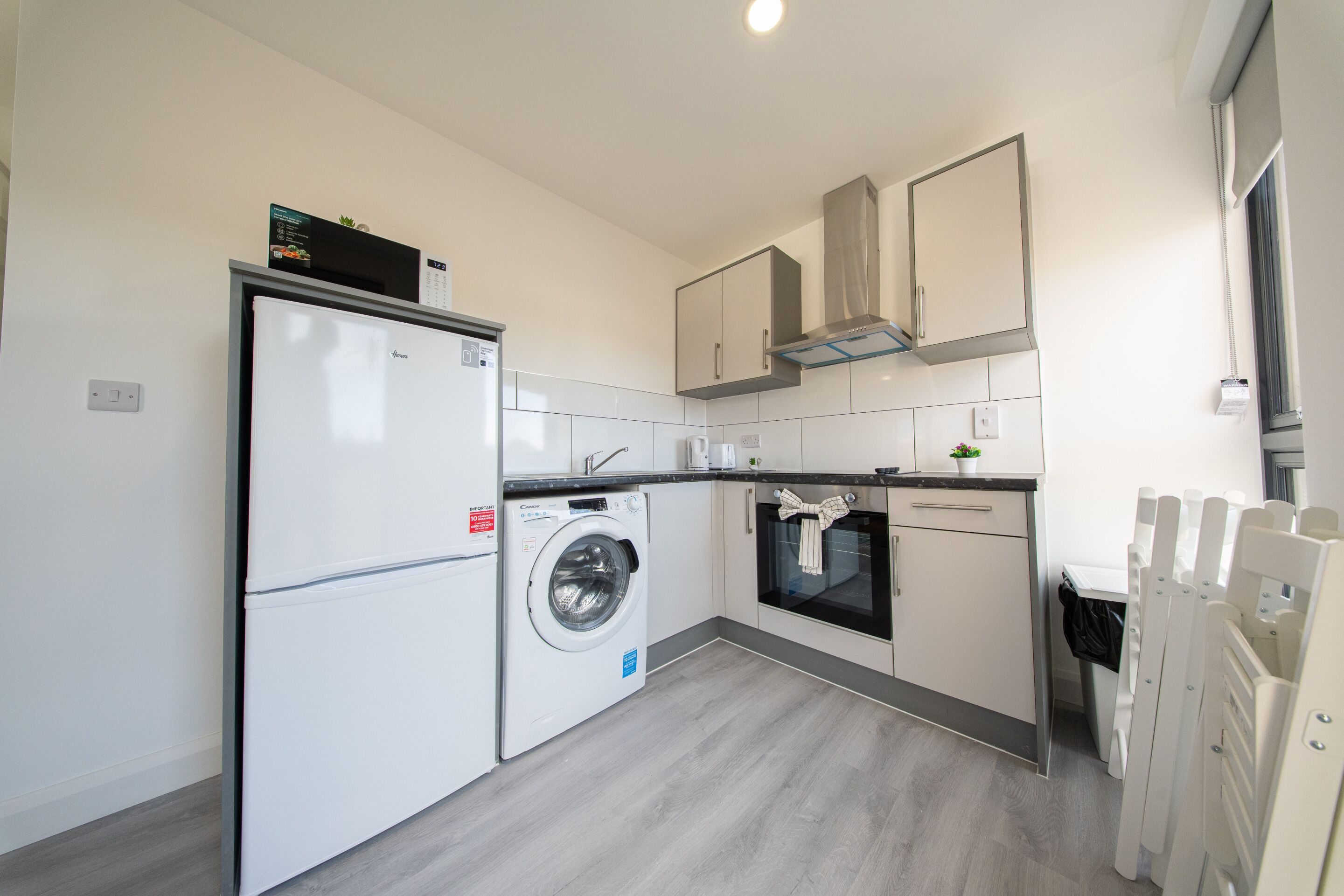 A compact kitchen with a refrigerator, washing machine, oven, and a microwave.