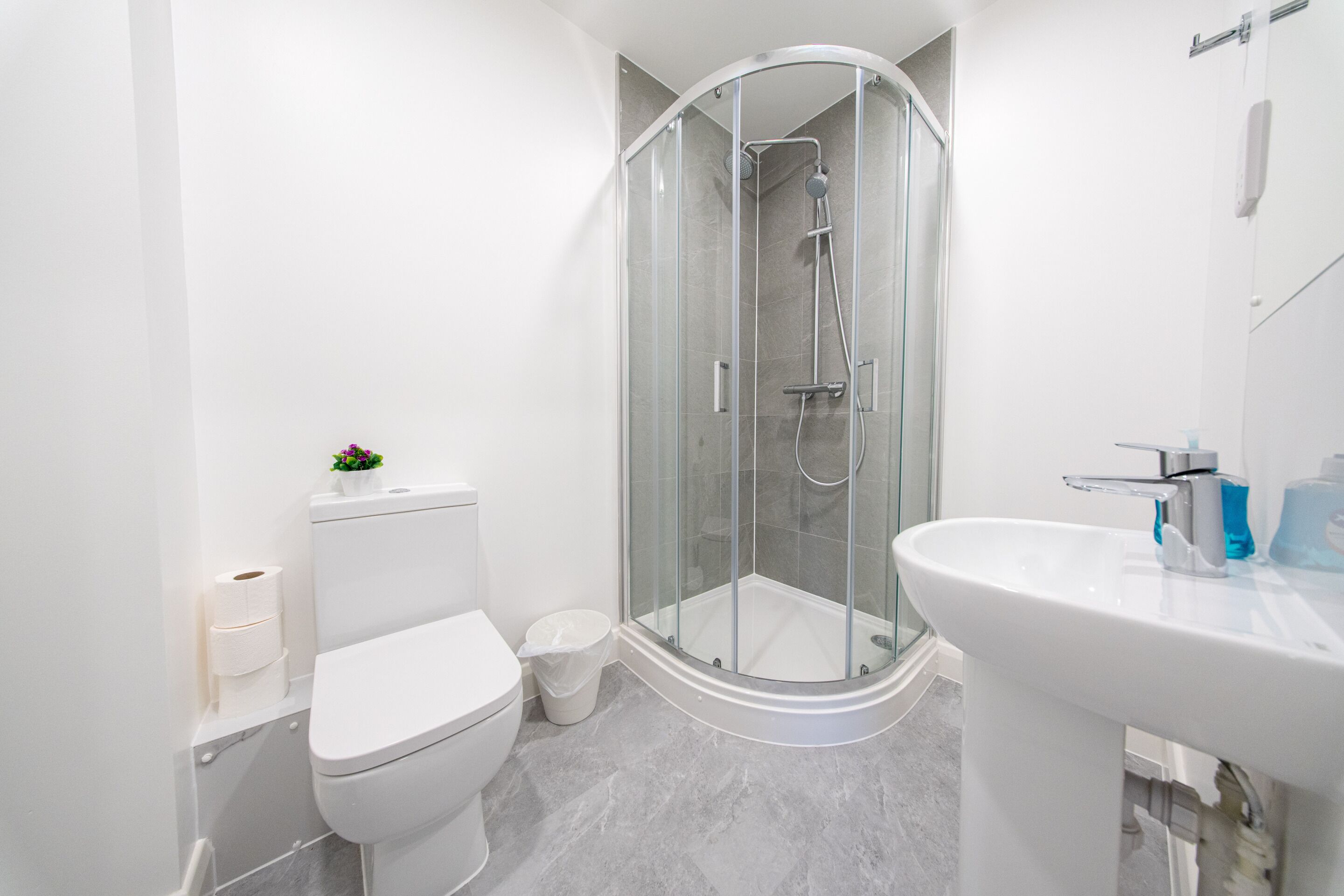 A modern bathroom with a glass-enclosed shower, a white toilet, and a sink with a mirror.