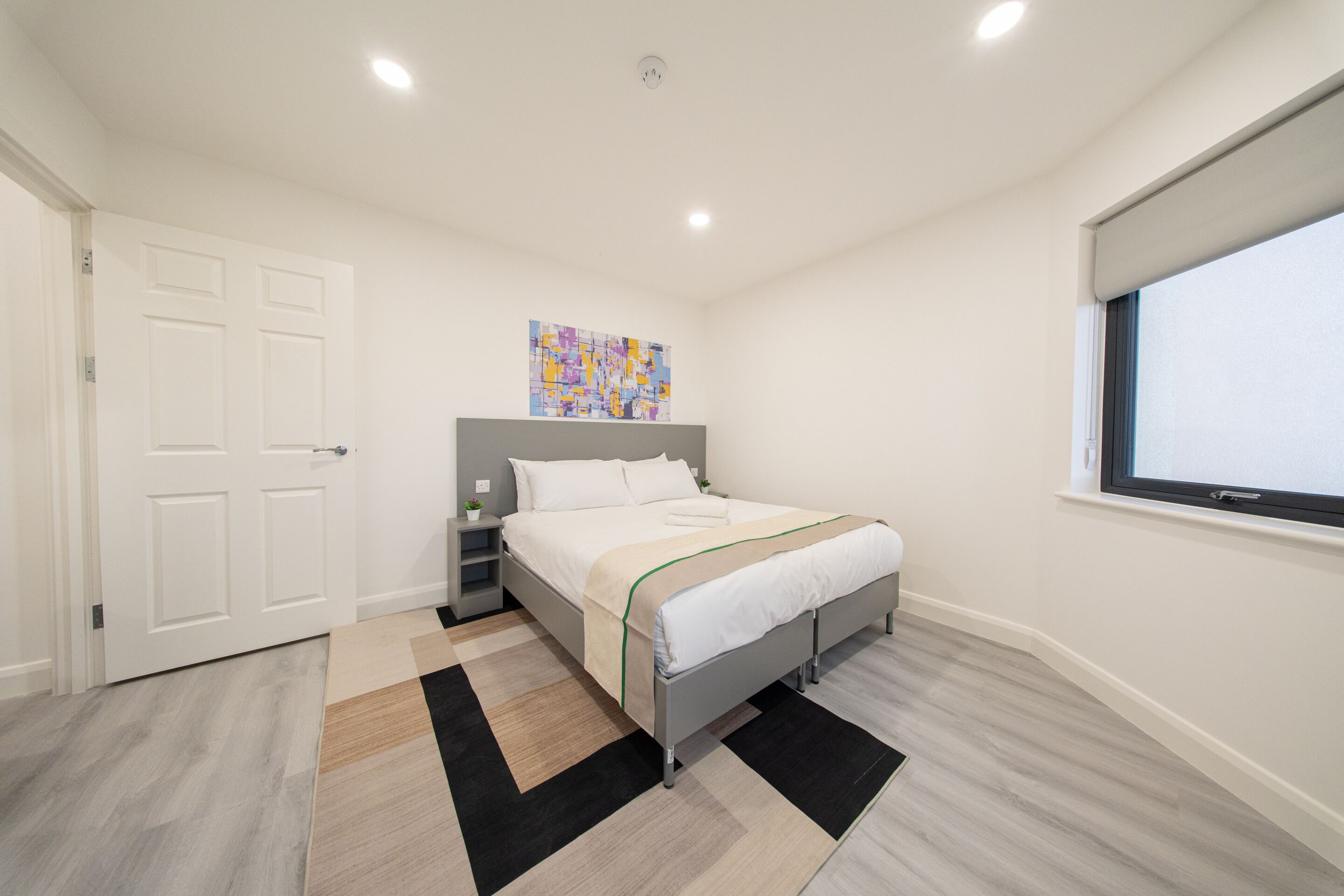 A modern bedroom with a bed, bedside tables, a window, and a door.