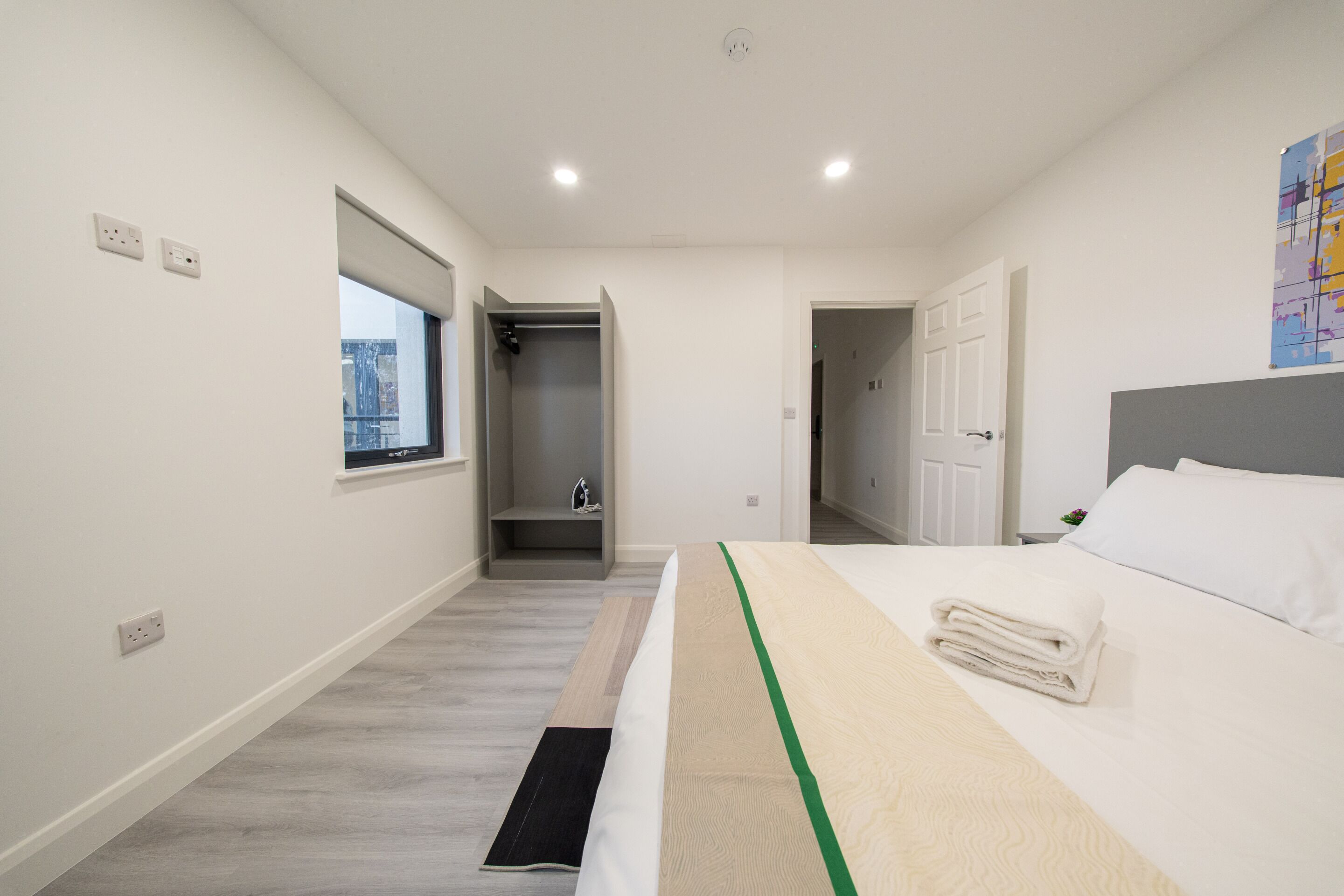 A modern hotel room with a bed, a window, a shower, and a door leading to another room.