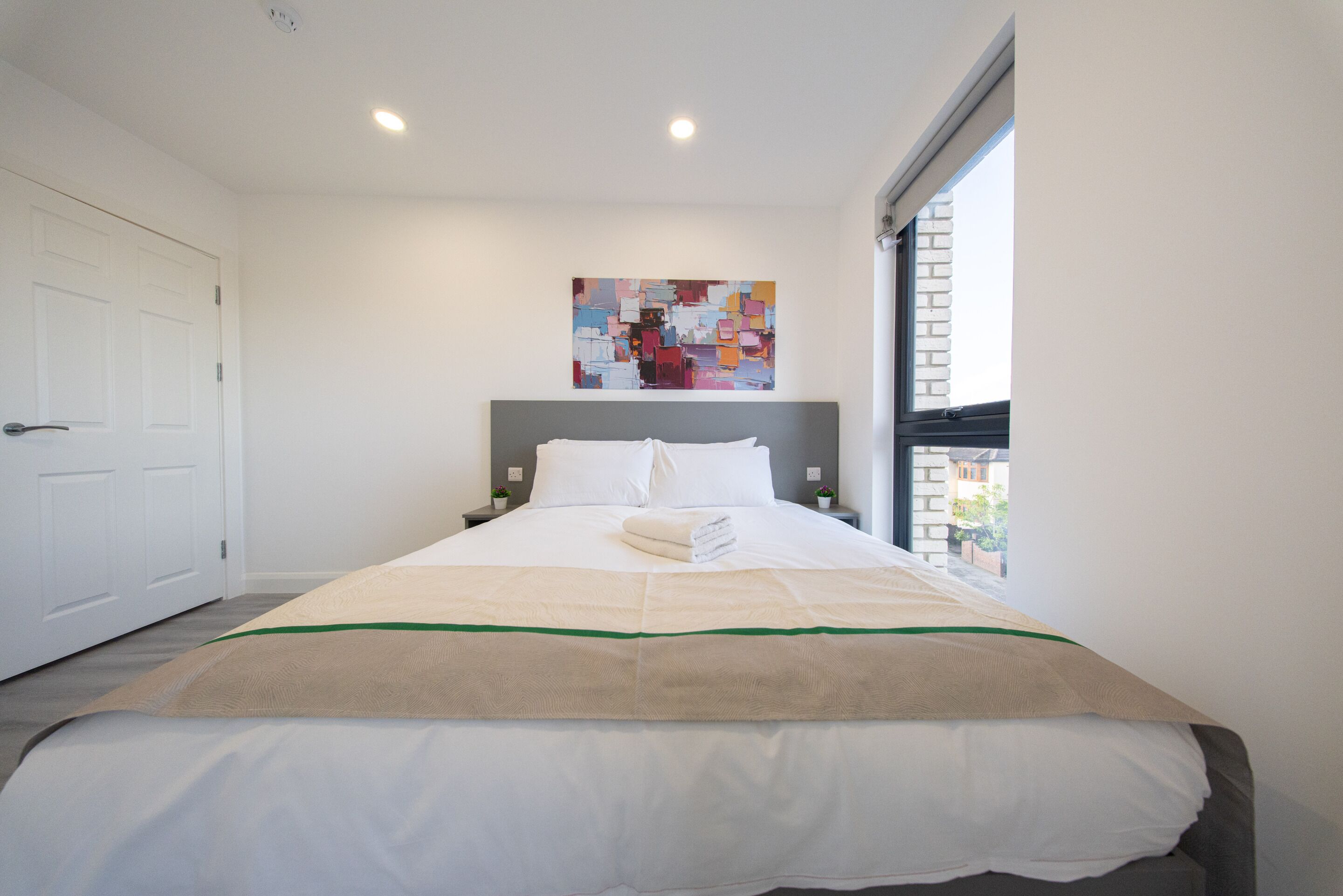 A hotel room with a bed, a painting on the wall, and a window.