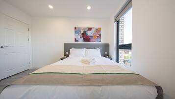 A hotel room with a bed, a painting on the wall, and a window.