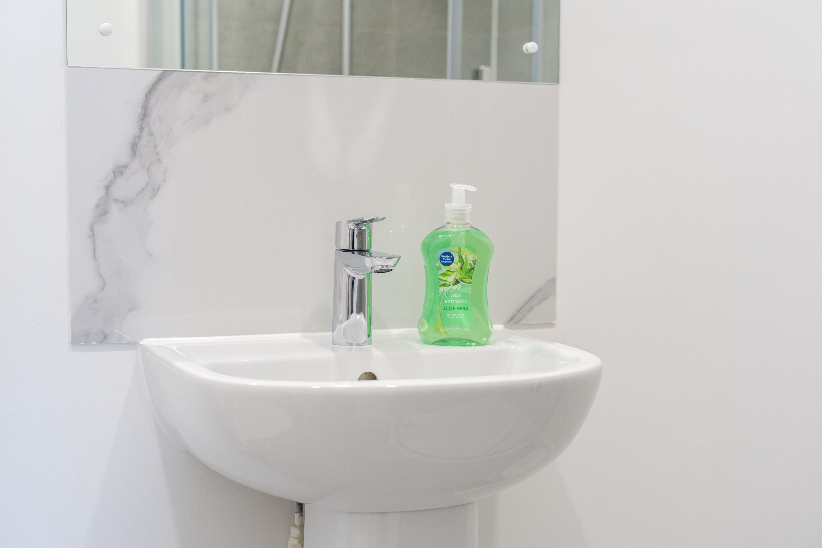A white bathroom sink with a chrome faucet and a green bottle of hand soap.