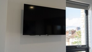 A flat-screen TV mounted on a wall in a room with a window. - Ilford Apartments on the Lane (Ilford)