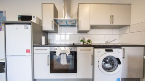 A compact kitchen with a refrigerator, oven, and washing machine. - Ilford Apartments on the Lane (Ilford)