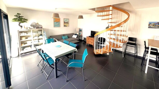 A modern living room with a dining area, a built-in bookshelf, a spiral staircase, and a large window. - Bright house in the heart of the village-100m from the ocean-6people (Angoulins)