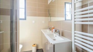 A modern bathroom with a glass shower enclosure, a white sink with a mirror, and a white towel rack. - Bright house in the heart of the village-100m from the ocean-6people (Angoulins)