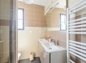A modern bathroom with a glass shower enclosure, a white sink with a mirror, and a white towel rack.