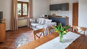 A compact living space with a kitchenette, a dining area with a table and chairs, and a sofa. - Luna Apartment (sleeps 4) (Rivoli veronese)