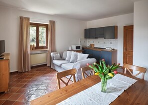 A compact living space with a kitchenette, a dining area with a table and chairs, and a sofa. - Luna Apartment (sleeps 4) (Rivoli veronese)