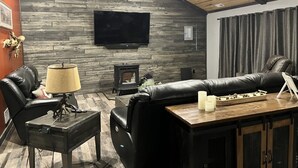 Una sala de estar acogedora con una pared de piedra, una chimenea, un sofá de cuero, una mesa de centro y un televisor de pantalla plana.