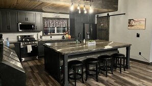 Una cocina moderna con armarios oscuros, una isla grande con taburetes, horno empotrado y una lámpara colgante.