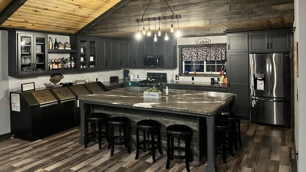 Una cocina moderna con armarios de madera oscura, una isla grande con taburetes de bar, un refrigerador de acero inoxidable y techo de madera.