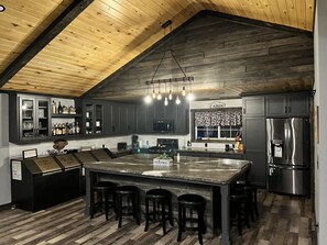 A modern kitchen with dark wood cabinets, a large island with bar stools, a stainless steel refrigerator, and a wooden ceiling. - Lake Nokomis Elegant Home-Family Friendly (Tomahawk)