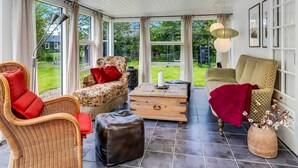 A sunroom with wicker furniture, a wooden coffee table, and a view of the garden. - 4 Star Holiday Home in Hemmet (Hemmet)