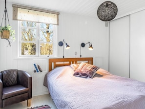 A bedroom with a bed, a chair, a window with a view of trees, and two wall-mounted lamps. - 4 Star Holiday Home in Hemmet (Hemmet)