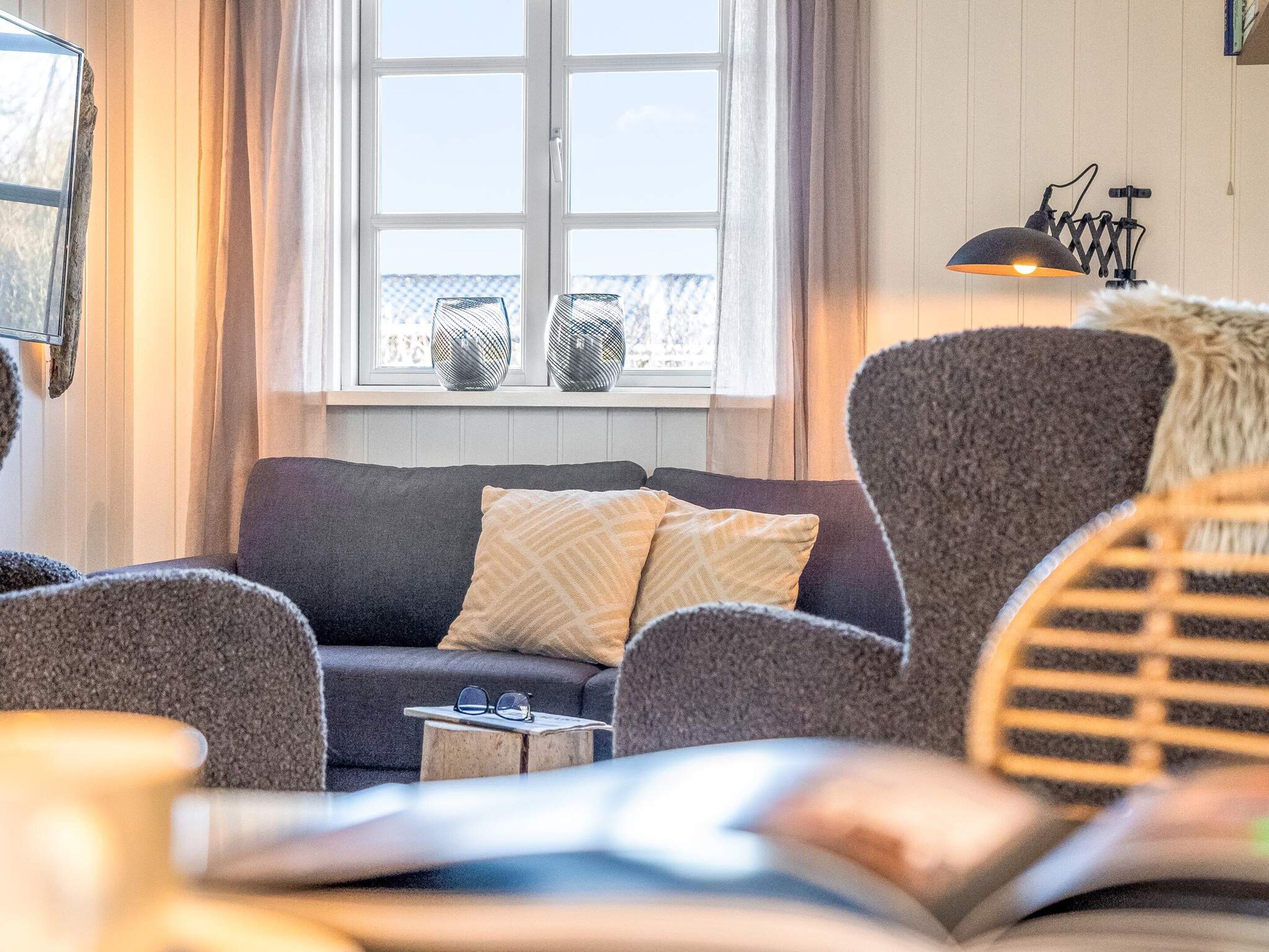 Un salon chaleureux avec un canapé, des fauteuils, une petite table d’appoint et une fenêtre agrémentée de vases décoratifs.