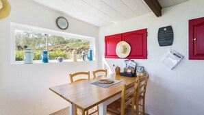 Un coin repas avec une table en bois, des chaises, une fenêtre donnant sur un paysage verdoyant et des meubles de rangement rouges.