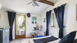 Une chambre à coucher comprenant un lit, un bureau, une chaise, un ventilateur de plafond et une vue sur l’extérieur.