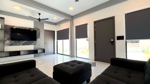 A modern living room with a flat-screen TV, dark-toned furniture, and large windows. - Ahiva Suites Goidhoo (Goidhoo)