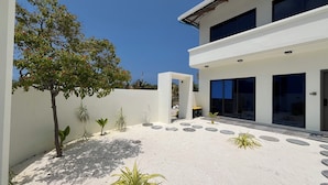 A modern building with a white exterior, large windows, and a paved courtyard with stepping stones and potted plants. - Ahiva Suites Goidhoo (Goidhoo)