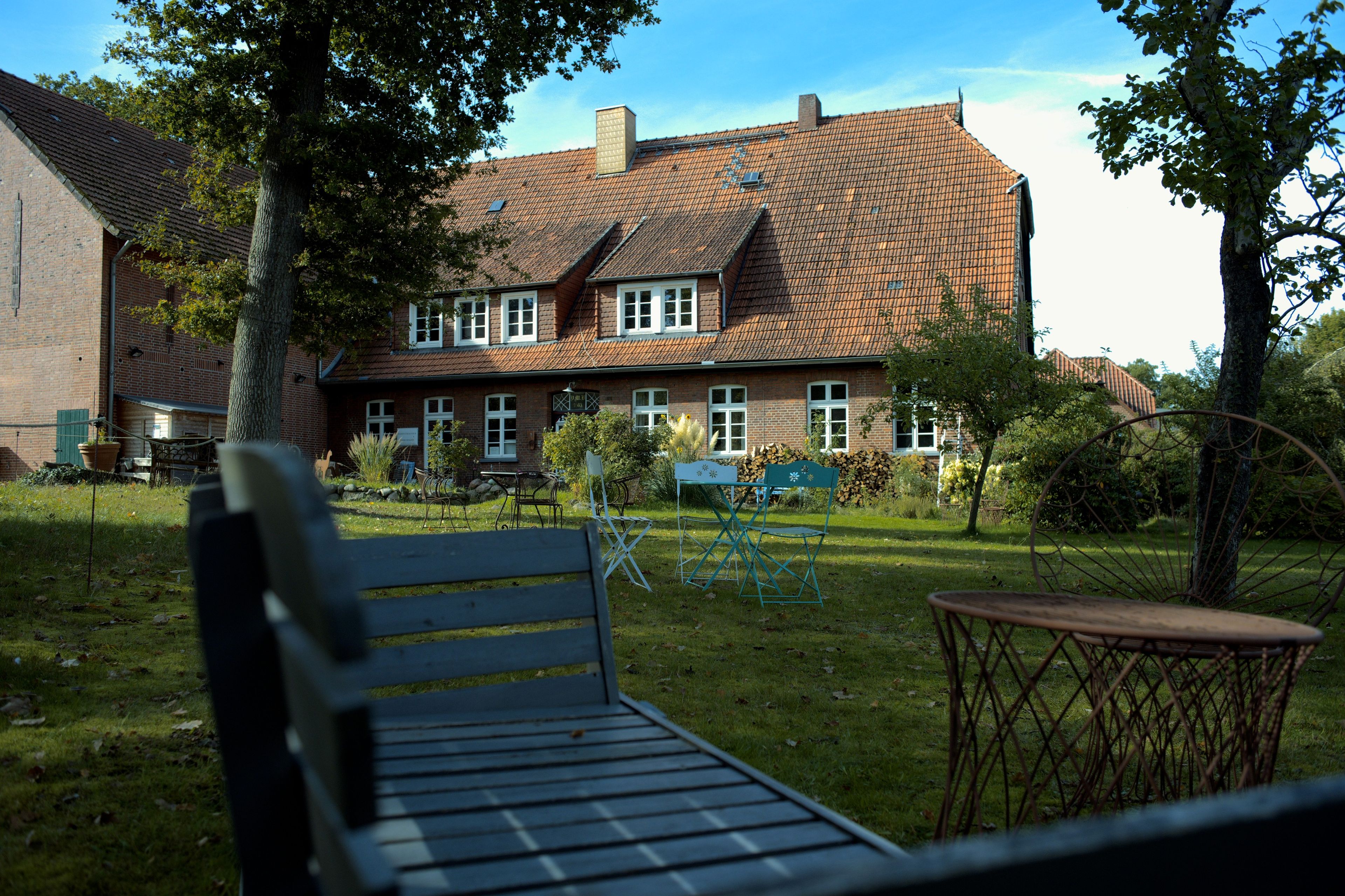 A brick building with a tiled roof, a bench, and a small table in a grassy yard.