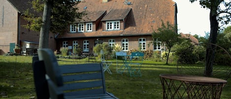 A brick building with a tiled roof, a bench, and a small table in a grassy yard.