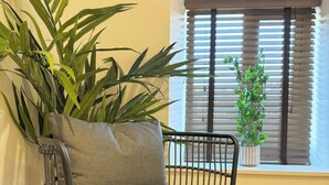 Una silla con asiento y respaldo tejidos, ubicada al lado de una planta grande en maceta.
