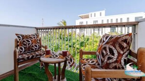 A balcony with two wooden chairs and a small table, each with patterned cushions.