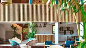 A spacious indoor area with a wooden ceiling, multiple seating areas with wicker furniture, and a central plant arrangement.