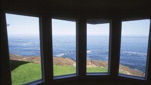 Una habitación con un ventanal grande que da a una costa rocosa y al océano.