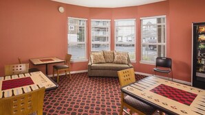 Una habitación con alfombra roja estampada, un sofá, una mesa con un tablero de ajedrez y un refrigerador con un menú.