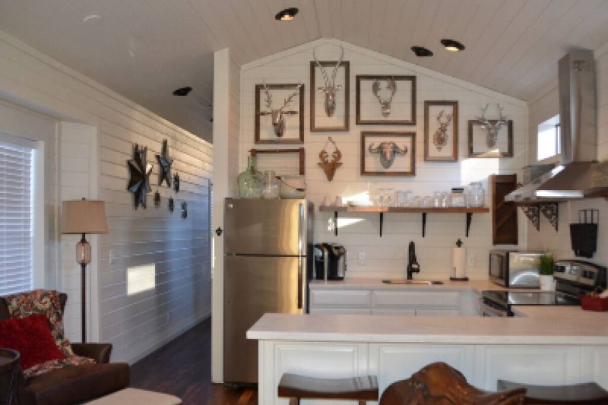 Una cocina con una isla central, muebles blancos y varios objetos decorativos en las paredes.