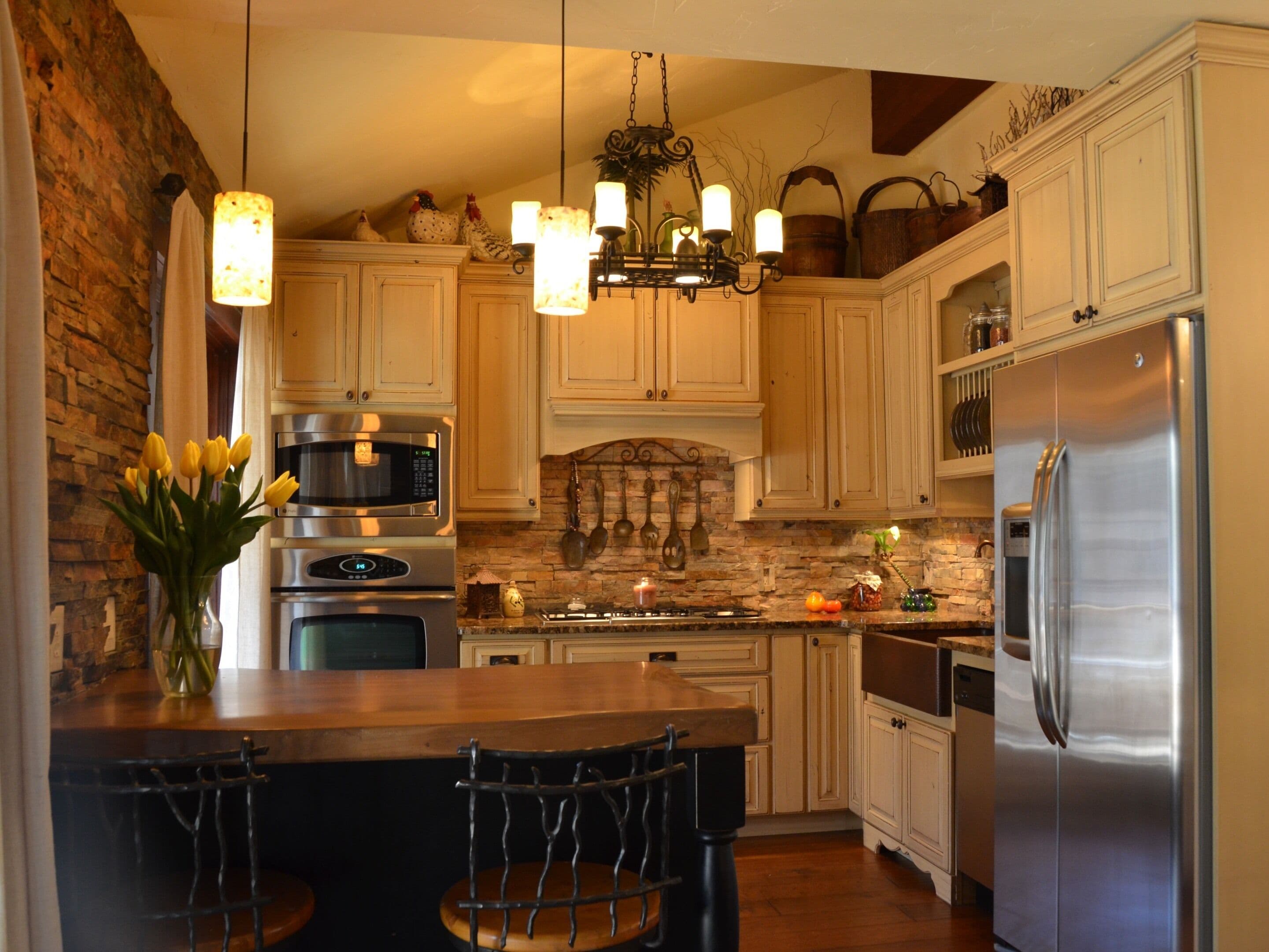 A kitchen with white cabinets, a stainless steel refrigerator, a built-in oven, a microwave, and a hanging light fixture.